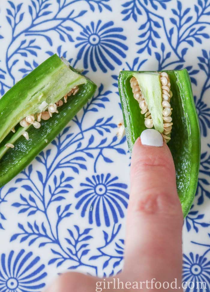 Finger pointing out the seeds and ribs in a cut jalapeno pepper.