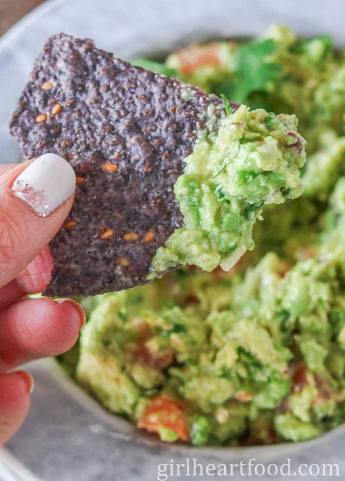 Hand holding a chip with guacamole on it.