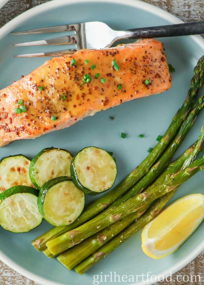 A fillet of honey mustard salmon with vegetables and lemon wedge on a blue plate.