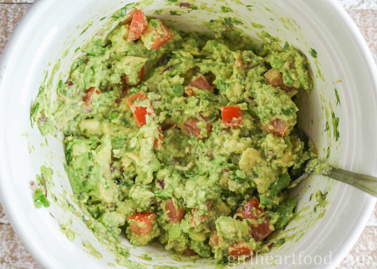 Mixing up guacamole in a white bowl with a spoon.