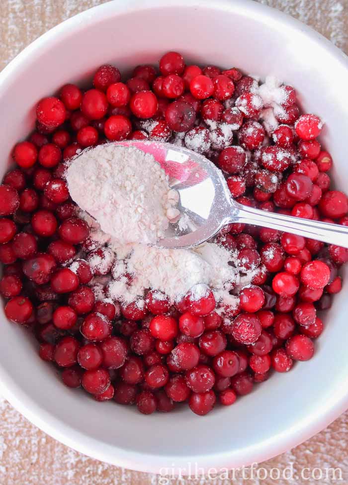 Spoon sprinkling flour over a bowl of partridgeberries.