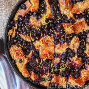 Blueberry bread pudding in a cast-iron skillet sprinkled with fresh lemon zest.