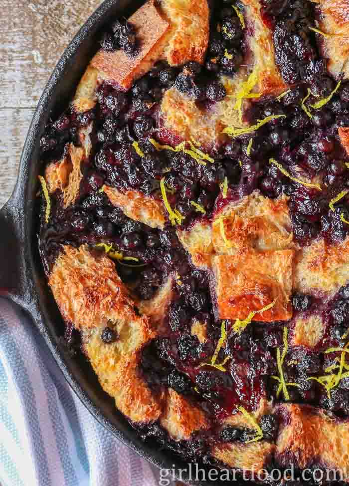 Blueberry bread pudding in a cast-iron skillet sprinkled with fresh lemon zest.