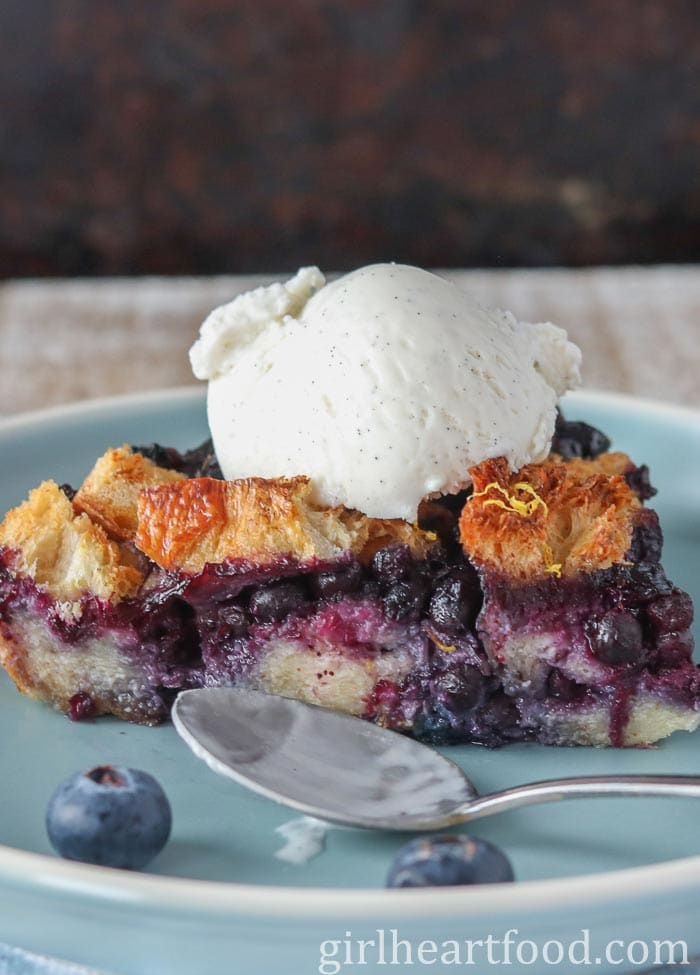 Portion of blueberry bread pudding topped with vanilla ice cream on a blue plate.