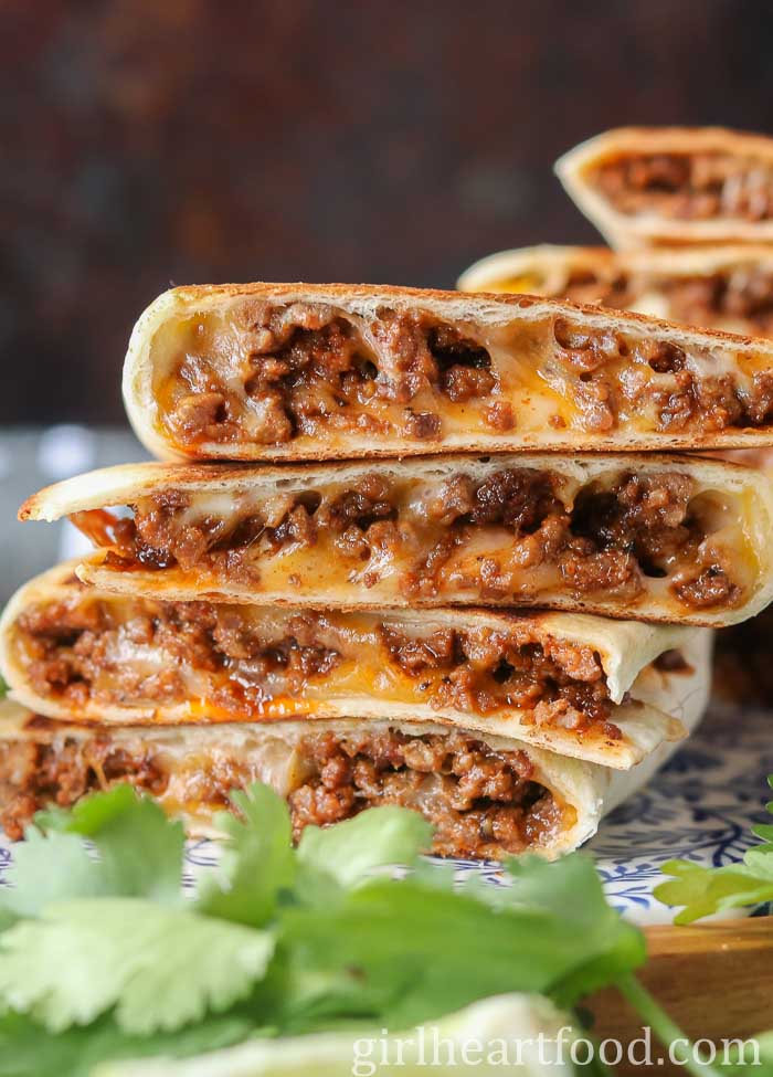 Stack of four cheesy ground beef quesadillas next to cilantro.