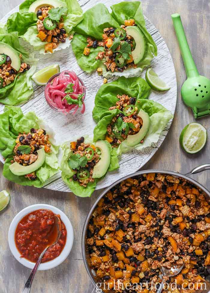 A plate of scrambled tofu lettuce wraps next to salsa and a pan with more tofu scramble in it.