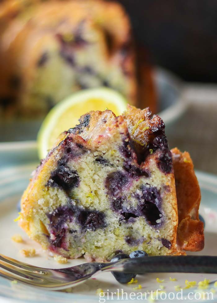 Piece of blueberry lemon cake on a blue plate with a fork.