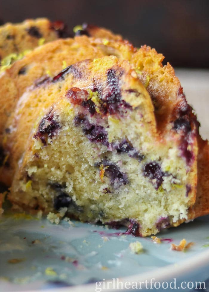 A cut blueberry lemon cake on a blue plate, showing the interior texture.