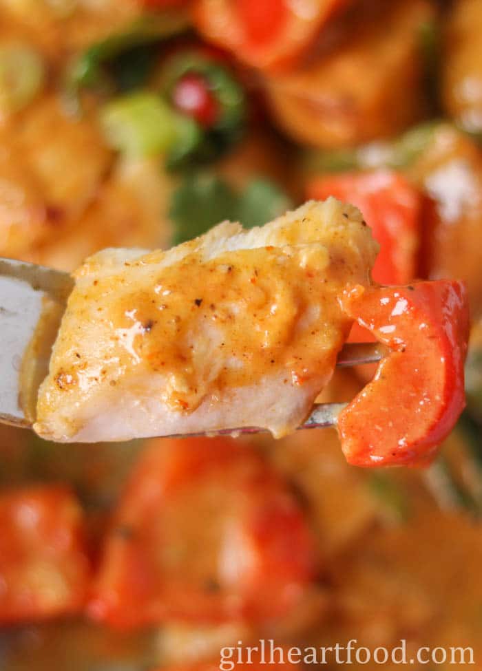 A forkful of curried white fish and red bell pepper.