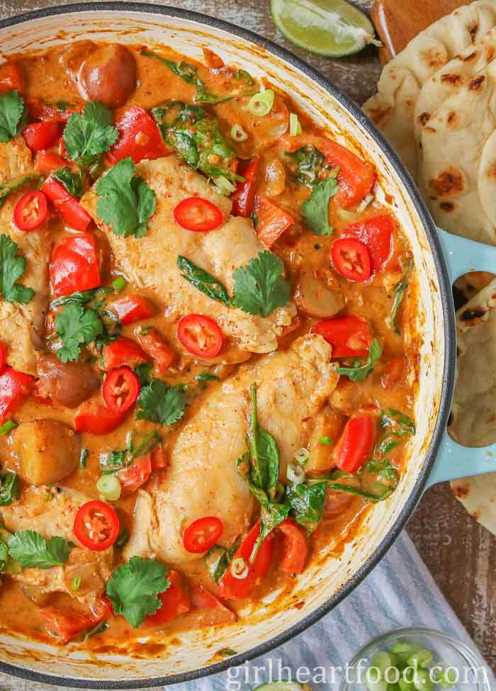 Close-up of fish curry in a pan garnished with cilantro, chili pepper and green onion.