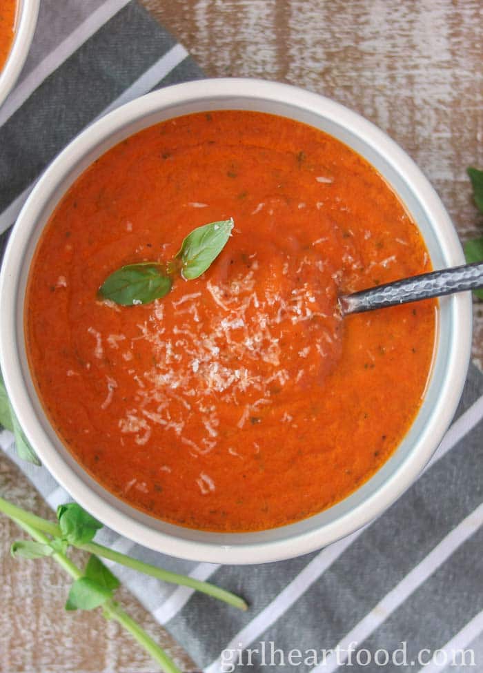 Bowl of tomato soup garnished with basil, Parmesan and oil.