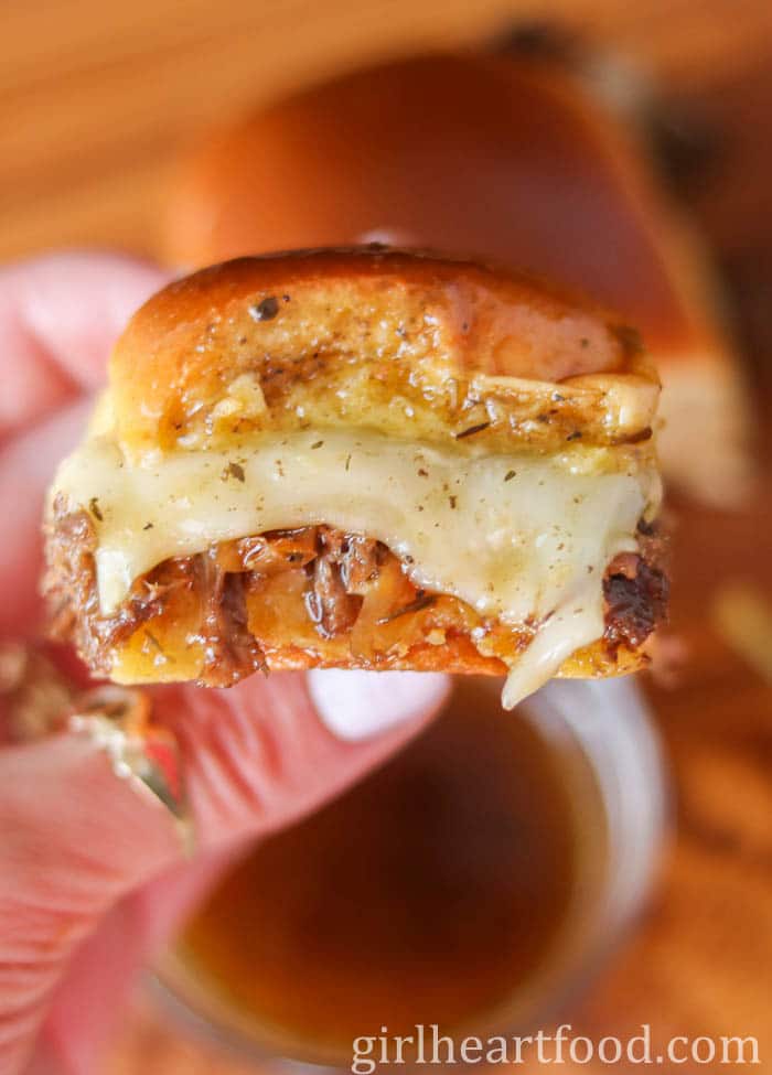 Hand holding a beef slider with cheese that has been dipped in au jus.