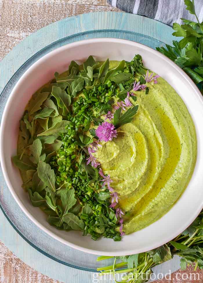 Bowl of green goddess hummus garnished with herbs, oil and chive flowers.