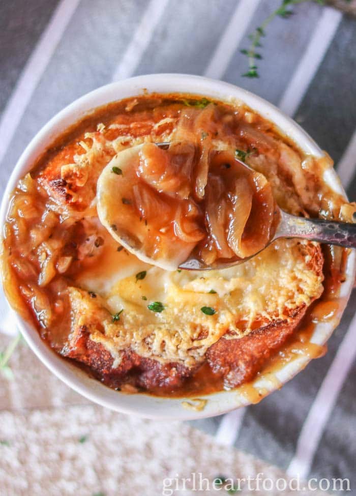 Spoonful of French onion soup held above a bowl of it.
