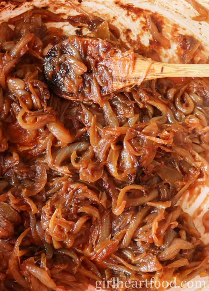 Caramelized onions in a pan being stirred by a wooden spoon.