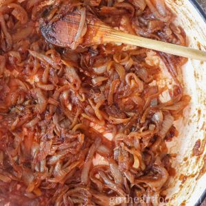 Caramelized onions in a pan being stirred by a wooden spoon.