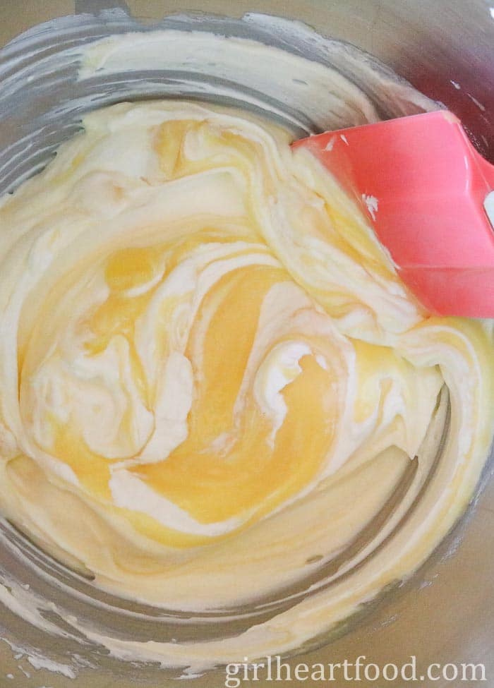 Using a pink spatula to fold lemon curd into whipped cream in a stainless steel bowl.