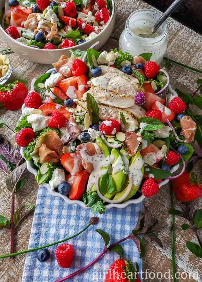 Bowl of green salad drizzled with dressing, sitting in front of another salad and jar of dressing.