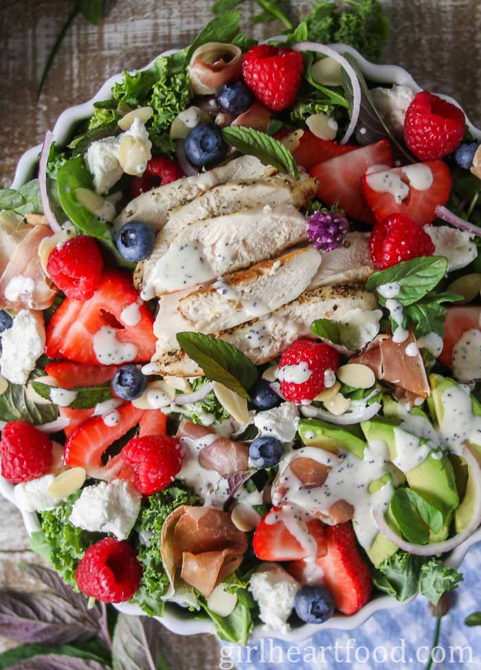 Close-up of a green salad with poppy seed dressing drizzled over top.