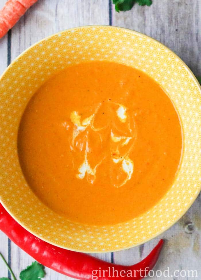 Bowl of curry carrot soup with a swirl of coconut milk on top.