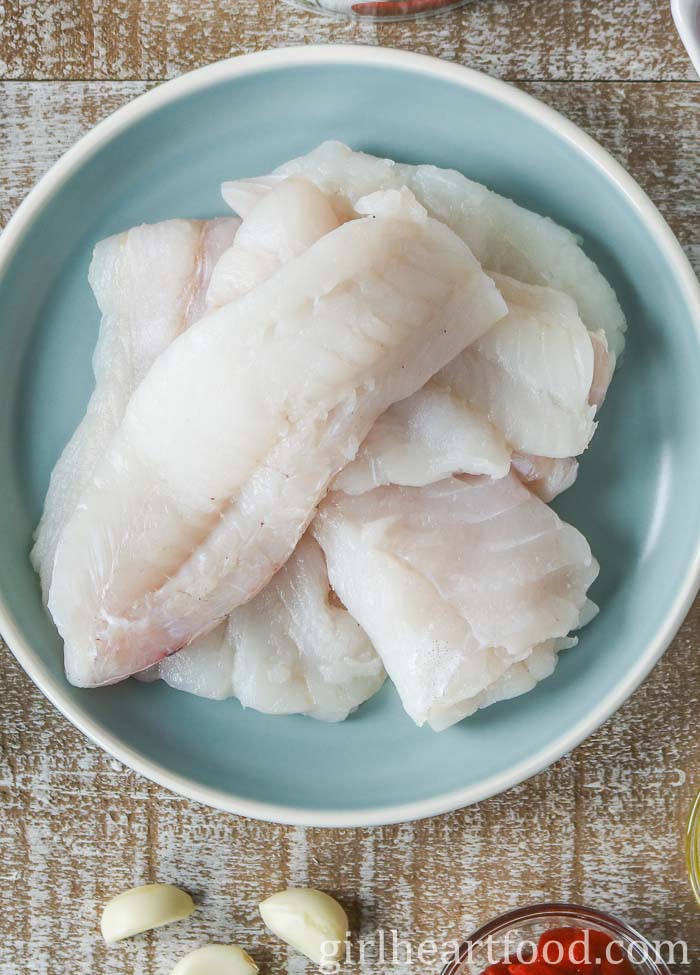 Uncooked cod fillets on a blue plate.