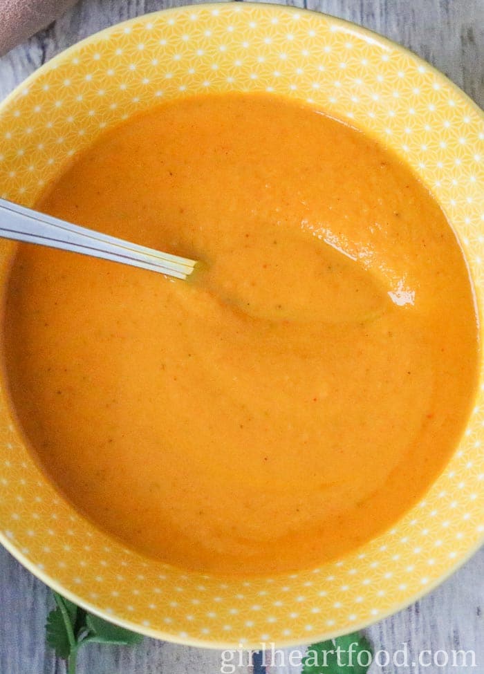 Spoon resting in a bowl of curry carrot soup.