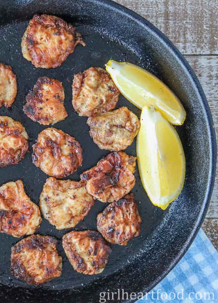 Pan-fried cod tongues and two lemon wedges in a cast-iron skillet.