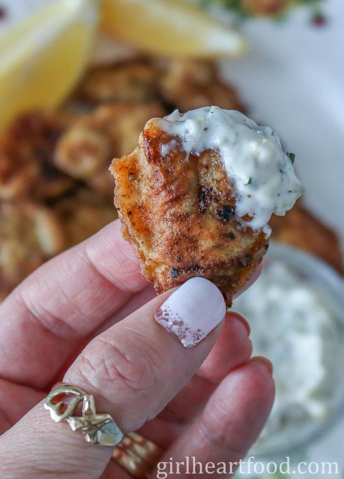 Hand holding a fried cod tongue that has been dipped in tartar sauce.