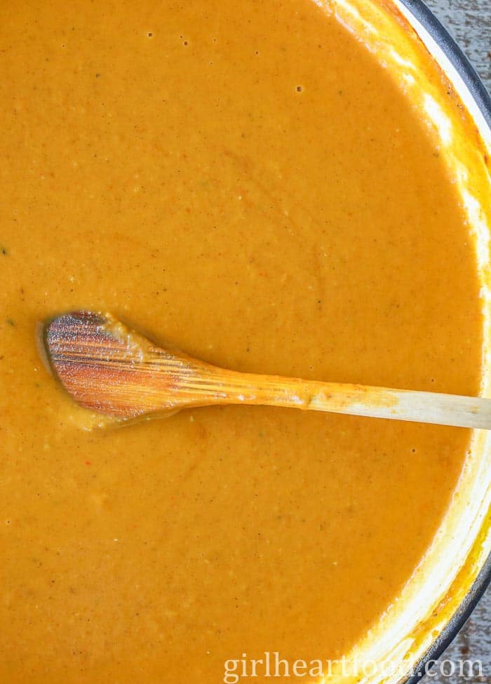 A pot of pumpkin soup being stirred by a wooden spoon.