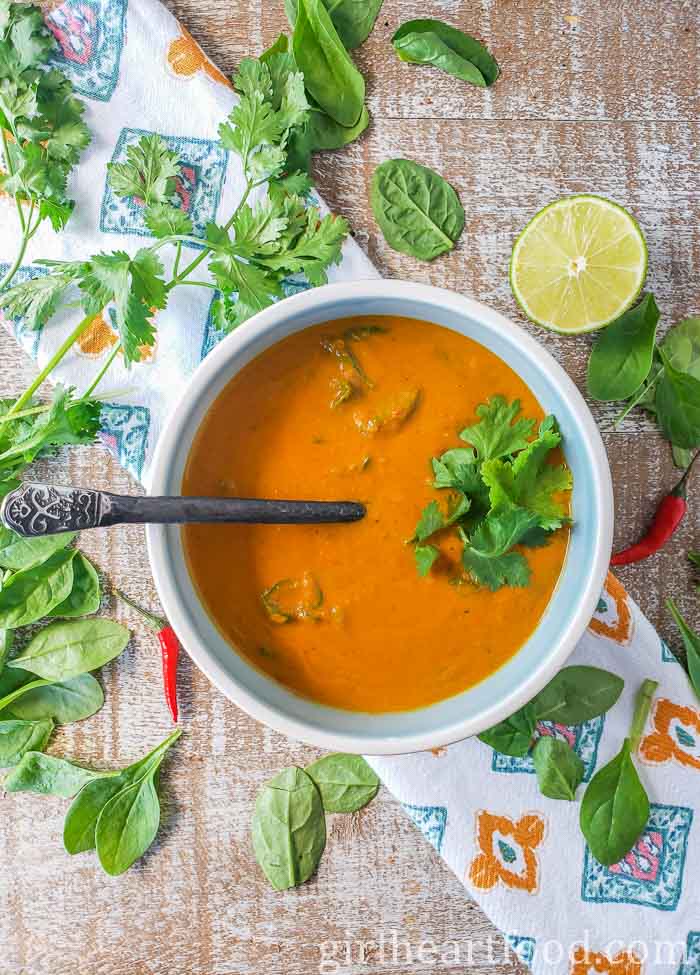 Bowl of pumpkin soup next to spinach, lime, chili peppers and cilantro.