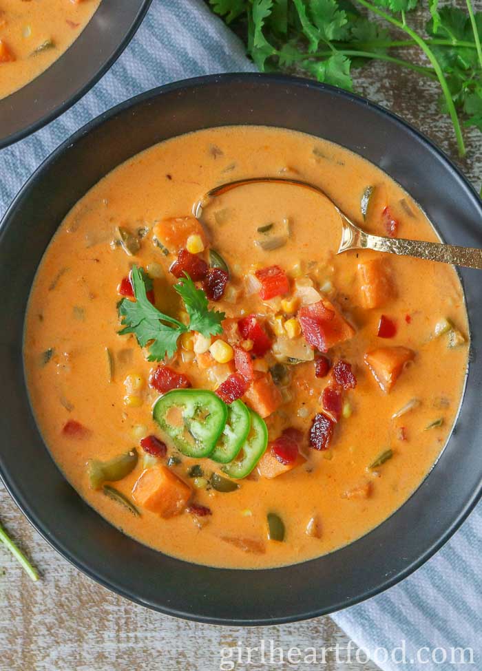 Bowl of corn soup garnished with bacon, jalapeno and cilantro.