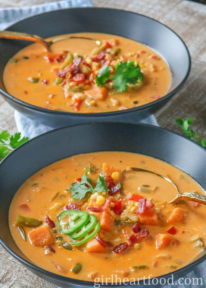 Two bowls of corn soup, each garnished with bacon, jalapeno and cilantro.