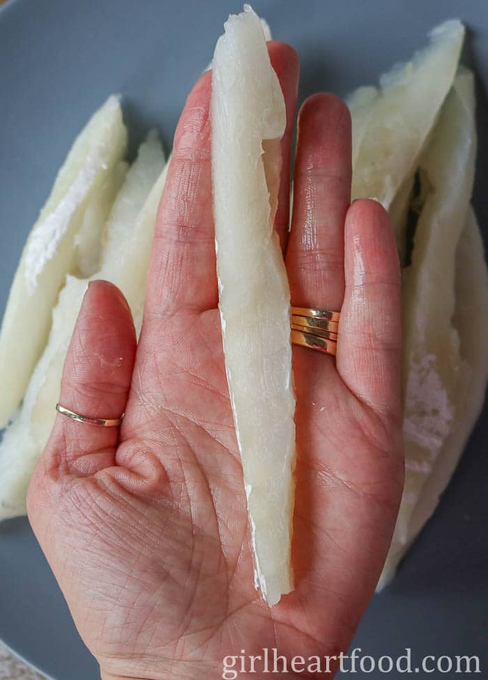 Hand holding a raw, thin strip of cod.