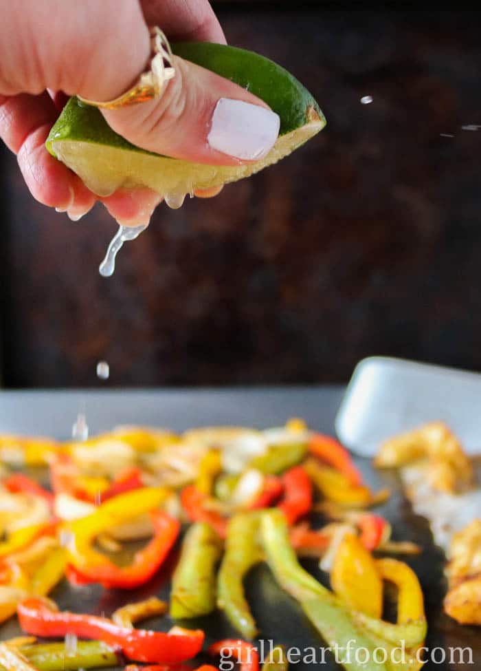 Hand squeezing lime over cooked bell pepper strips.