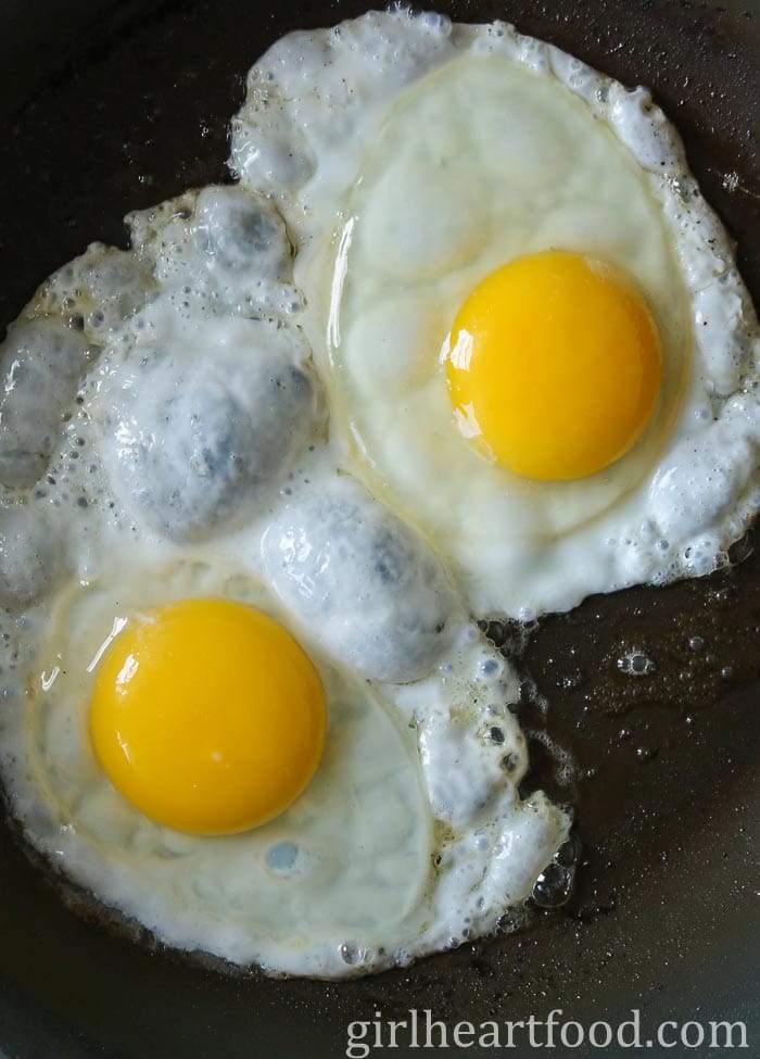 Two eggs frying in a frying pan.