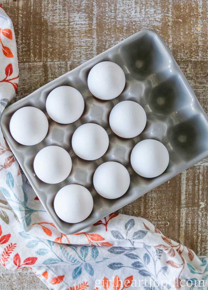 Eggs in a grey glass carton next to a tea towel.