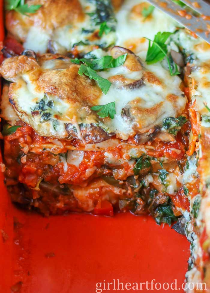 Close-up of veggie lasagna in a pan with a piece cut out.