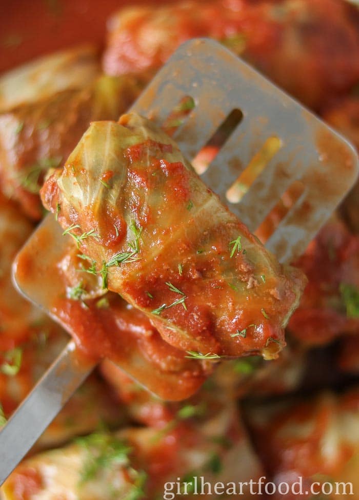 Cabbage roll with tomato sauce and dill, sitting on a spatula.