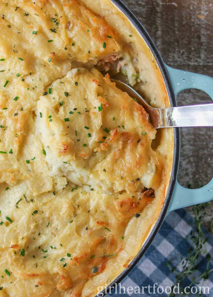Large serving spoon dunked into a pan of fish pie.