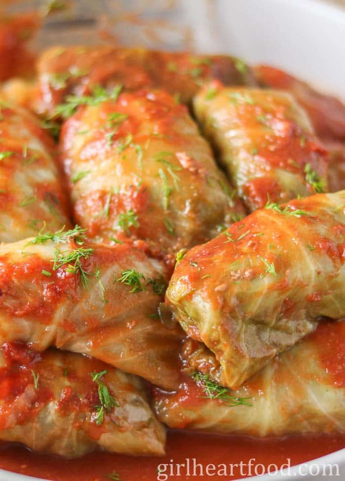 Dish of old-fashioned cabbage rolls with tomato sauce and dill garnish.