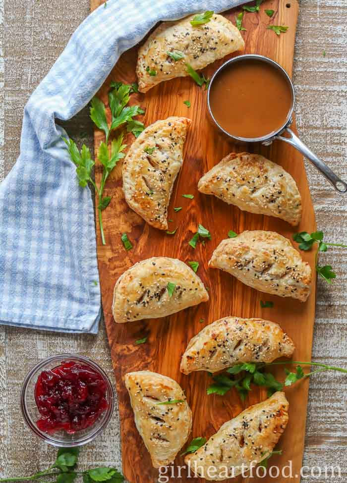 Savoury hand pies next to a pot of gravy, bowl of cranberry sauce, parsley and a tea towel.