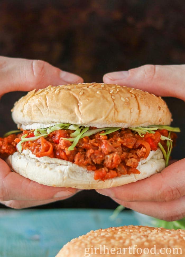 Two hands holding a sloppy joe sandwich made with ground turkey.