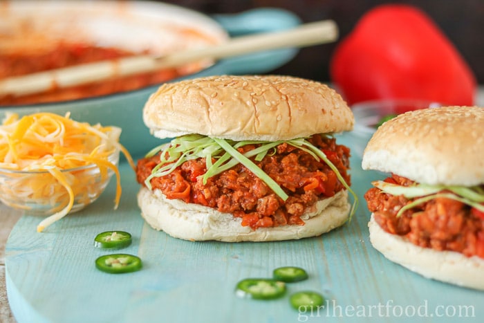 Two turkey sloppy joes alongside some slices of jalapeno pepper and shredded cheese.