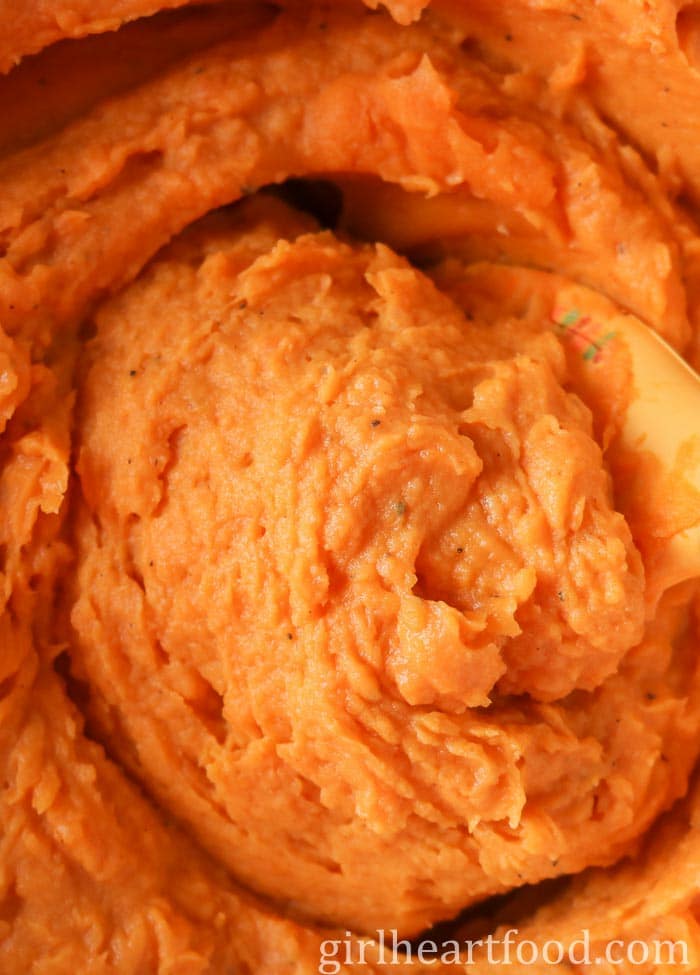 Close-up of creamy sweet potatoes being stirred by a spatula.