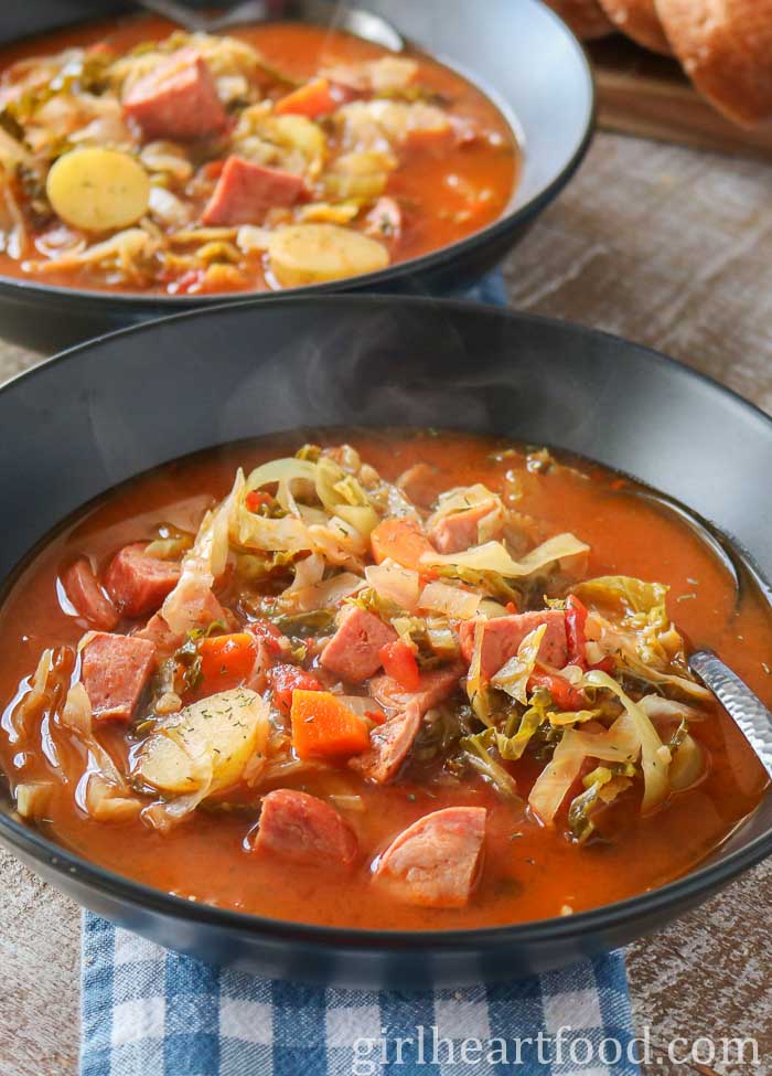 Two bowls of cabbage soup with sausage and potatoes, one bowl in front of the other.