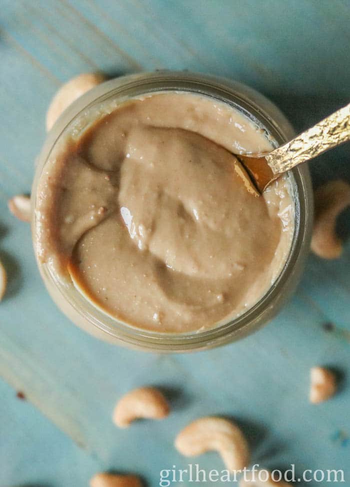 Jar of smooth cashew butter with a gold spoon dunked into it.