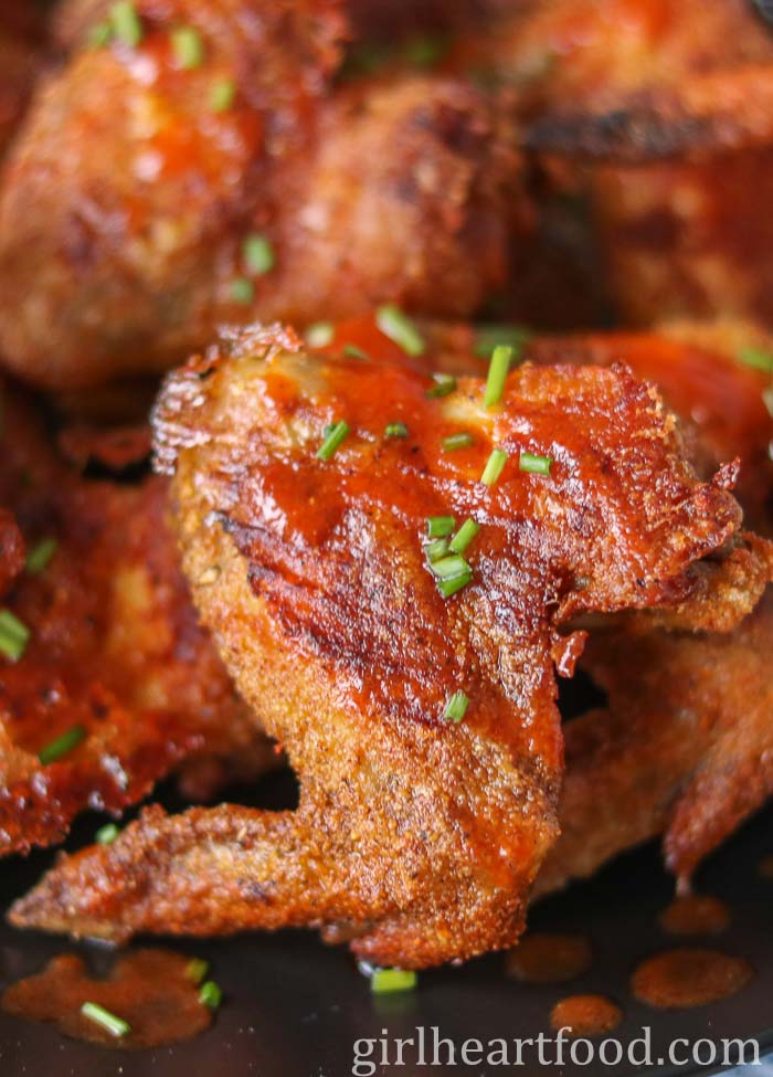 Close-up of spicy chicken wings with chive garnish.