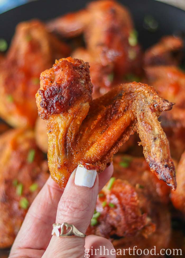 Hand holding a crispy baked chicken wing.