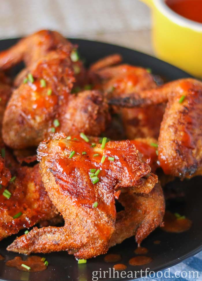 Crispy baked chicken wings with sauce and chives on a black plate.