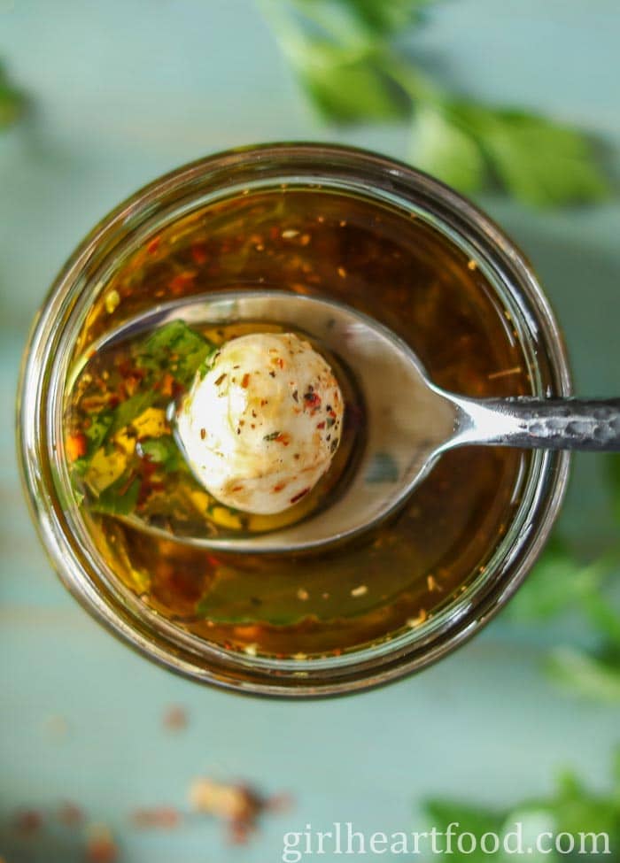 Spoon scooping up a marinated mozzarella ball from a jar of them.